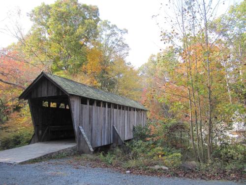 A rustic wooden covered bridge surrounded by colorful autumn foliage and gravel path.