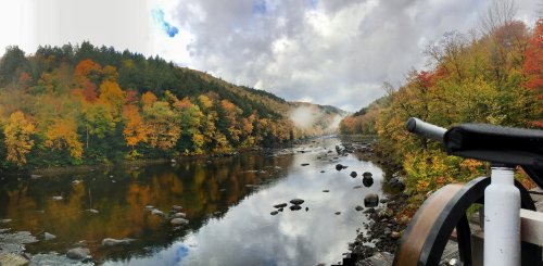 Scenic view of a river surrounded by vibrant autumn foliage and misty mountains under a cloudy sky.