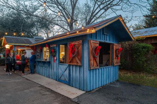 A blue wooden kiosk decorated with wreaths, surrounded by trees and string lights, with people outside.