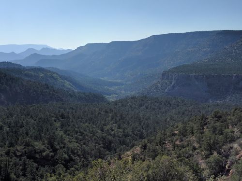 A panoramic view of a lush green valley surrounded by mountains under a clear blue sky.