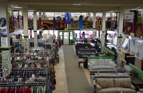 A spacious thrift store interior with clothing racks, shoes, and furniture displayed across multiple levels.