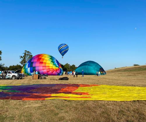 Colorful hot air balloons being inflated on a grassy field under a clear blue sky, with people preparing nearby.