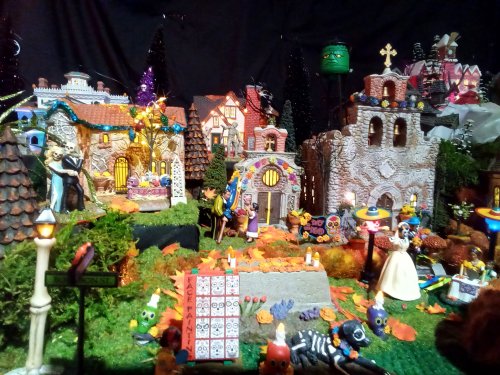 A colorful Halloween village scene with decorated houses, spooky figures, and autumn leaves.