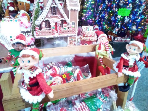 Colorful holiday display featuring elf dolls and gingerbread decorations, with a festive backdrop of lights.