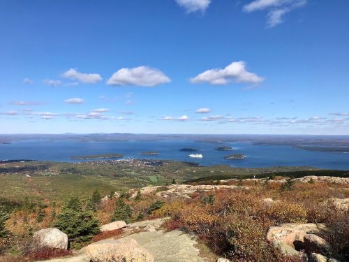 A panoramic view of a blue lake surrounded by islands and green hills under a clear sky with scattered clouds.