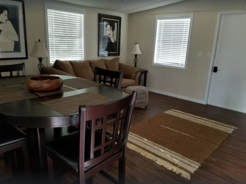 A cozy living space featuring a dining table, chairs, a sofa, lamps, and a textured rug on wooden flooring.