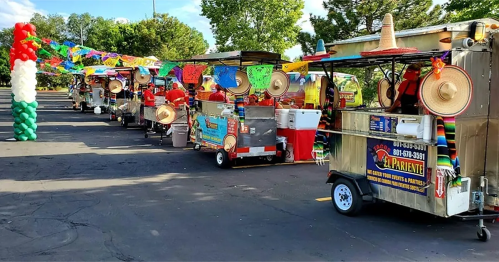 A row of colorful food carts decorated with sombreros and festive banners in a sunny outdoor setting.