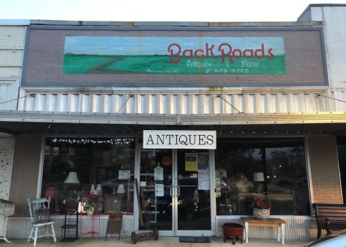 Front view of "Back Roads Antiques & Decor" store, featuring a sign and display of various antique items in the window.