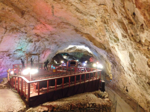 A colorful cave interior featuring a stage with musicians and lights, surrounded by rocky walls.