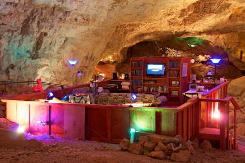 Cozy cave interior with a living area, bookshelves, a TV, and colorful lighting, creating a unique underground space.