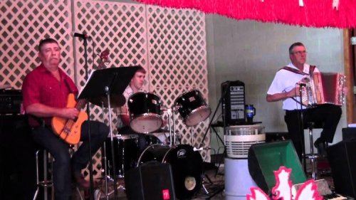 A band performs on stage with a guitarist, drummer, and accordion player at a lively event.