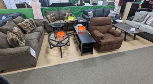 A furniture display featuring various sofas, coffee tables, and recliners with price tags in a store setting.