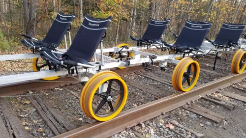 A row of four wheeled rail bikes on a train track, featuring comfortable seats and bright yellow wheels.