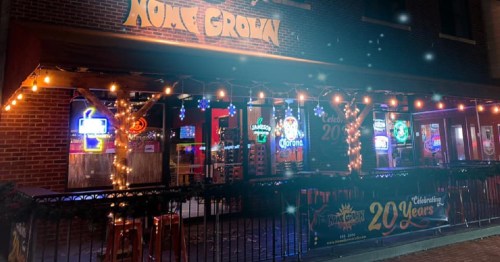 A festive bar exterior with string lights, neon signs, and a banner celebrating 20 years in business.