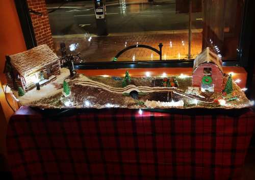 A festive display featuring two gingerbread houses on a snowy landscape, adorned with lights and miniature trees.