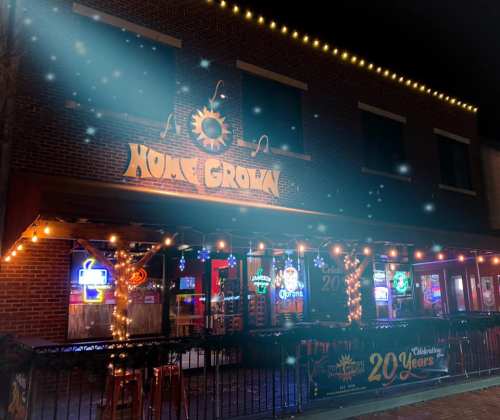 A cozy bar named "Home Grown" adorned with festive lights, celebrating 20 years, on a nighttime street.