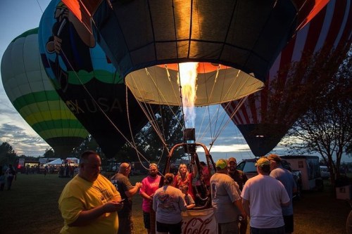 A hot air balloon is being inflated at dawn, with people gathered around and colorful balloons in the background.
