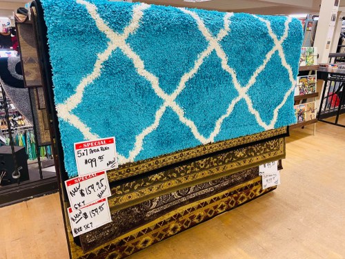 A display of area rugs in a store, featuring a blue shag rug with a white pattern and two other patterned rugs below.