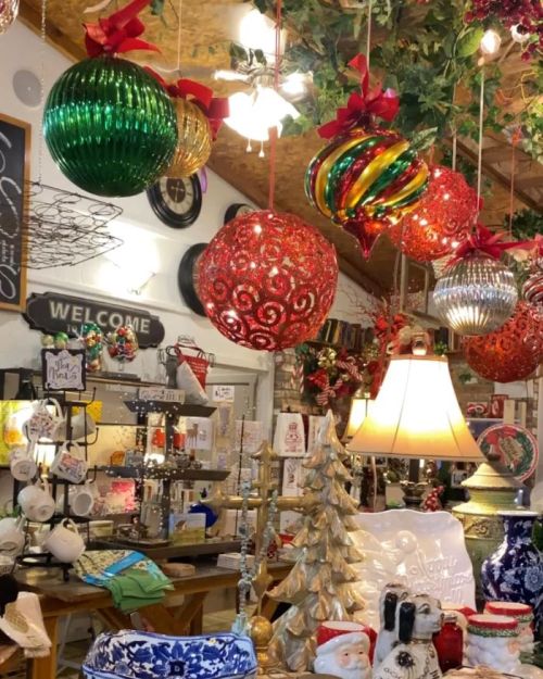 Colorful Christmas ornaments hang from the ceiling in a festive shop filled with holiday decorations and gifts.