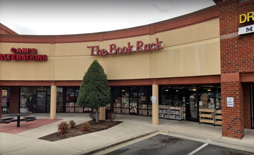 Exterior view of a bookstore named "The Book Rack" in a shopping plaza, with a tree and nearby businesses visible.