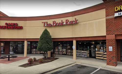 Exterior view of a bookstore named "The Book Rack" in a shopping plaza, with a tree and nearby businesses visible.