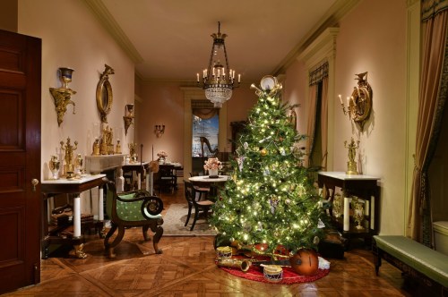 A beautifully decorated Christmas tree with lights and gifts in an elegant, vintage-style room.