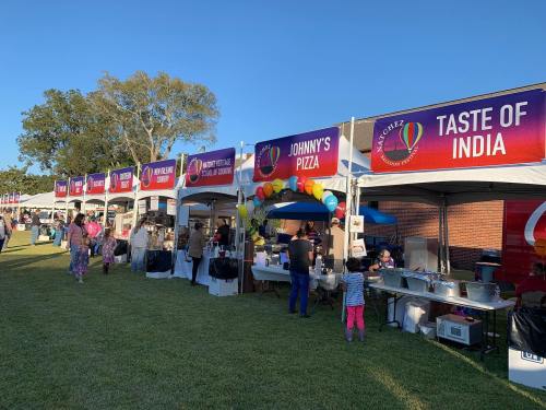 Food festival scene with various vendor tents, including "Johnny's Pizza" and "Taste of India," set in a grassy area.