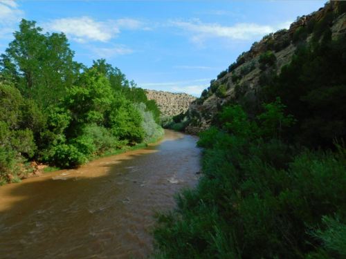 A winding river flows through a lush green landscape, surrounded by rocky hills and blue skies.