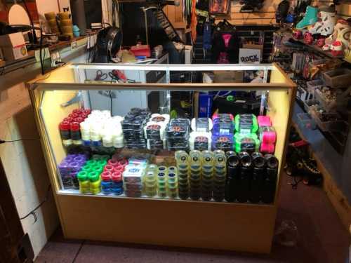 Display case filled with colorful skate wheels and accessories in a shop, surrounded by various sports equipment.