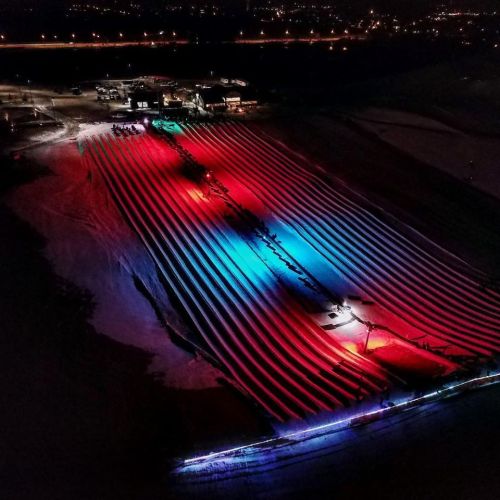 Aerial view of illuminated fields with colorful lights creating patterns against a dark landscape at night.