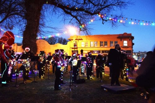 A festive band performs outdoors, adorned with Christmas lights, under a twilight sky with colorful decorations.
