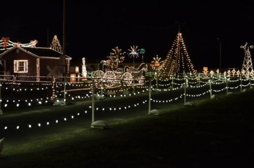 A festive display of colorful Christmas lights adorning houses and trees along a dark road.