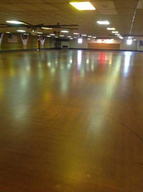 Empty roller skating rink with a polished wooden floor and colorful lights reflecting off the surface.