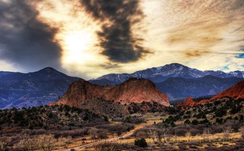 A dramatic landscape featuring rugged mountains, a rocky outcrop, and a cloudy sky at sunset.