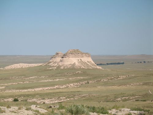 A flat-topped butte rises from a vast, grassy plain under a clear blue sky.