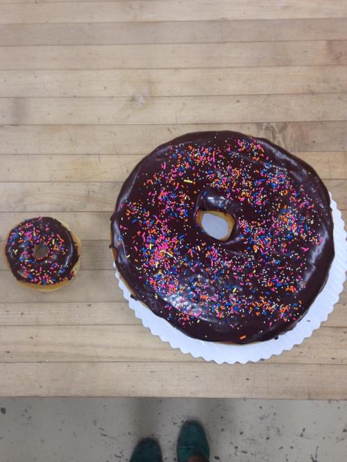 A large chocolate donut with colorful sprinkles next to a small donut on a wooden surface.