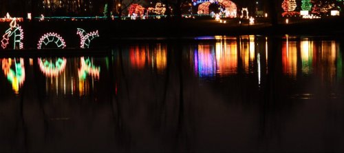 Colorful holiday lights reflect on a calm lake at night, creating a festive and serene atmosphere.