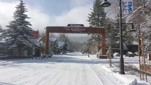 Snow-covered street with a wooden welcome arch and trees, creating a winter scene in a quaint village.