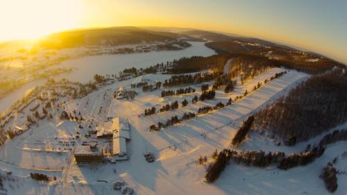 Aerial view of a snowy landscape at sunset, featuring a river, forested hills, and a ski resort.