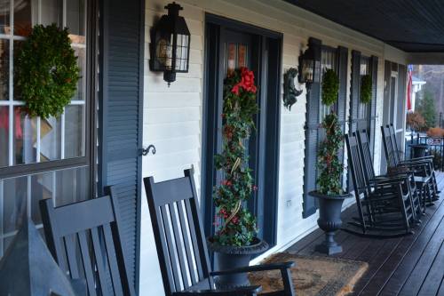 A cozy porch with rocking chairs, holiday wreaths, and festive decorations on a charming white house.