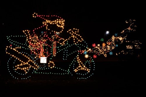Colorful holiday lights depict Santa on a motorcycle, surrounded by festive decorations in a nighttime setting.