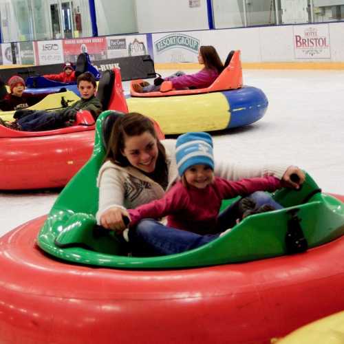 A group of children and adults enjoy bumper cars on ice, smiling and having fun in colorful inflatable vehicles.