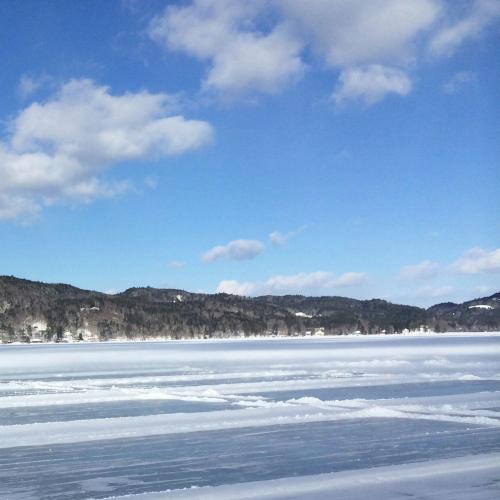 A serene winter landscape featuring a frozen lake, snow-covered shorelines, and a clear blue sky with fluffy clouds.