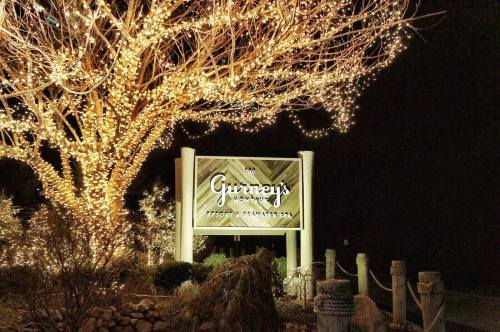 A sign for Gurney's Montauk Resort illuminated by festive lights, surrounded by trees and landscaping at night.