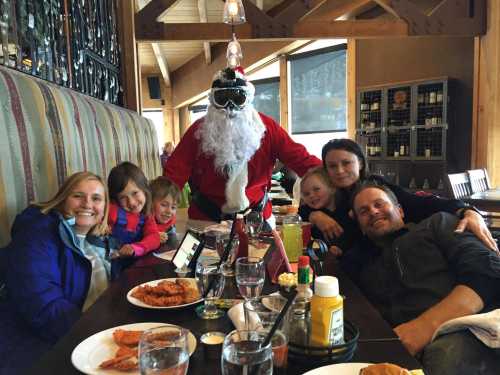 A group of smiling people, including a Santa figure, enjoying a meal together at a restaurant.