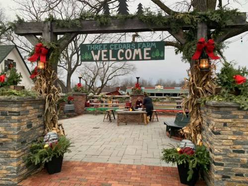 Entrance to Three Cedars Farm, decorated with holiday wreaths and lanterns, welcoming visitors to a festive outdoor space.