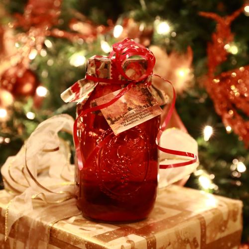 A festive red jar with a ribbon sits on a gift, surrounded by a decorated Christmas tree and twinkling lights.