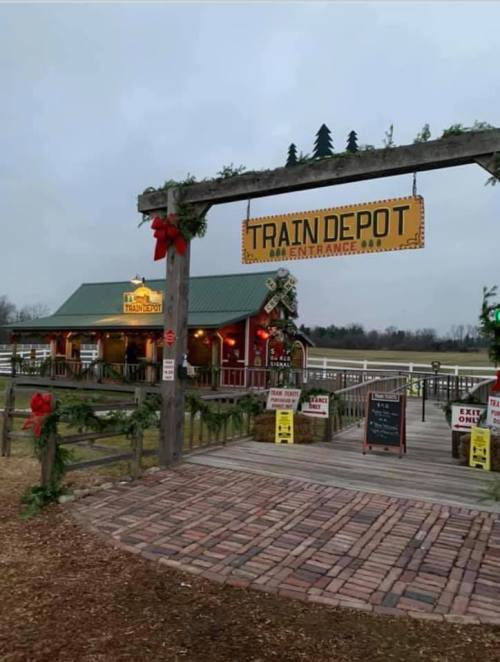 A rustic entrance to a train depot decorated with holiday wreaths, leading to a cozy building in a rural setting.