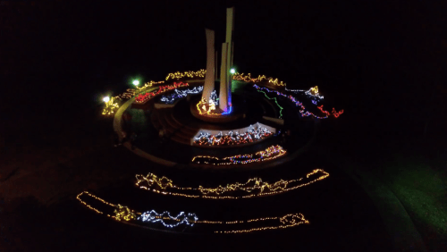 Aerial view of a monument illuminated with colorful lights at night, surrounded by decorative light patterns.