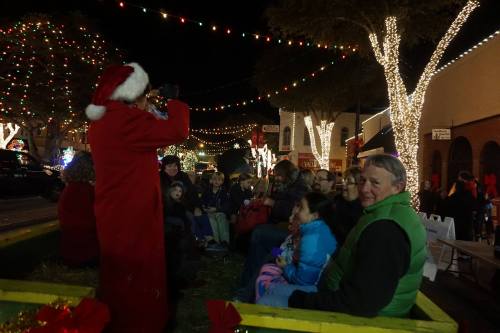 A festive scene with people in holiday attire enjoying a nighttime event, surrounded by colorful lights and decorations.